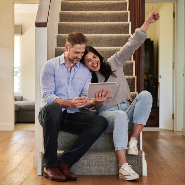 A couple sitting on the steps of their new home using a tablet computer.