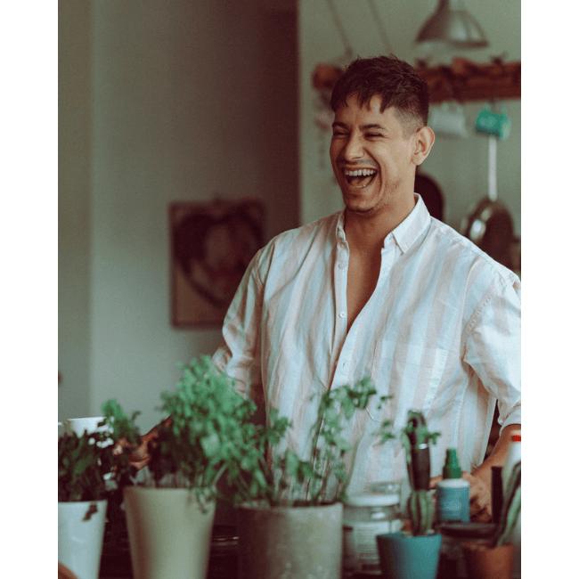 A man smiling in front of a kitchen with potted plants.